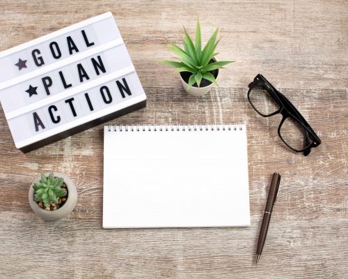 Goal, Plan, Action text on light box and Notebooks on wooden table. Business motivation, management, or inspiration. Planning concept.